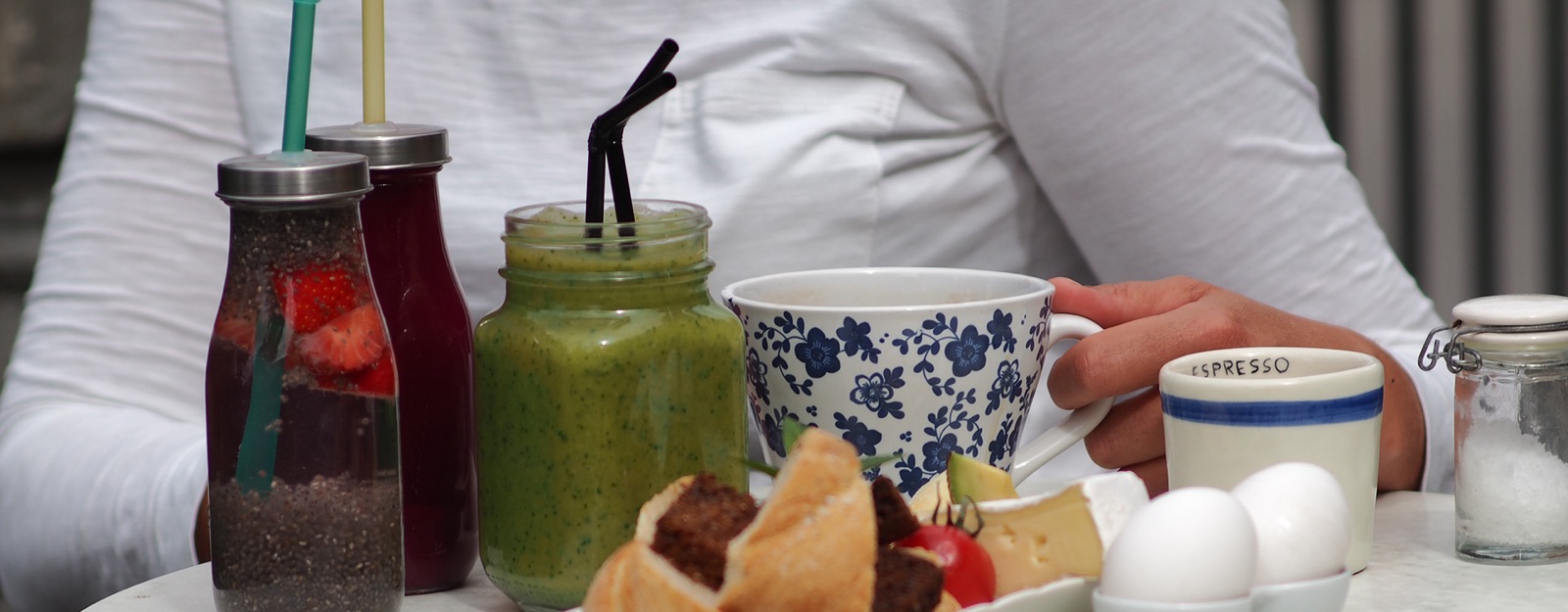 Juicer och smoothies i glasburkar, kaffekoppar och smörgåsar på ett dukat bord
