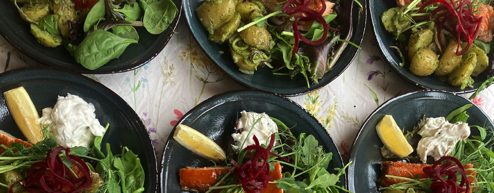 Dagens rätter uppifrån: sallad, fisk och grönsaker på mörka tallrikar